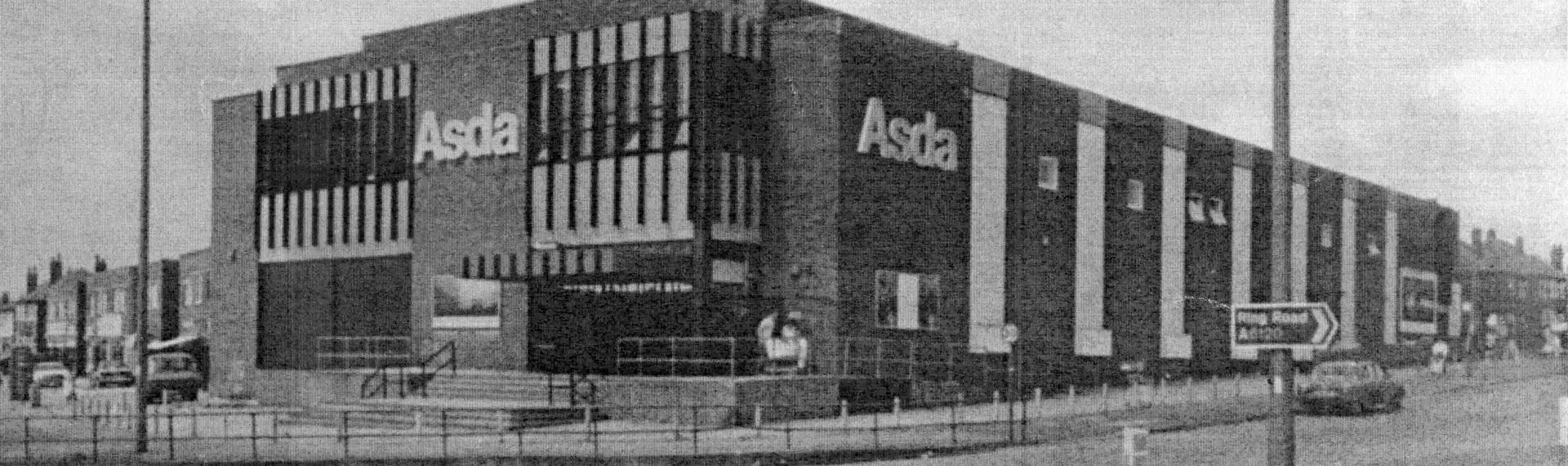 Black and white image of a two story brick building with ASDA logo on side and front